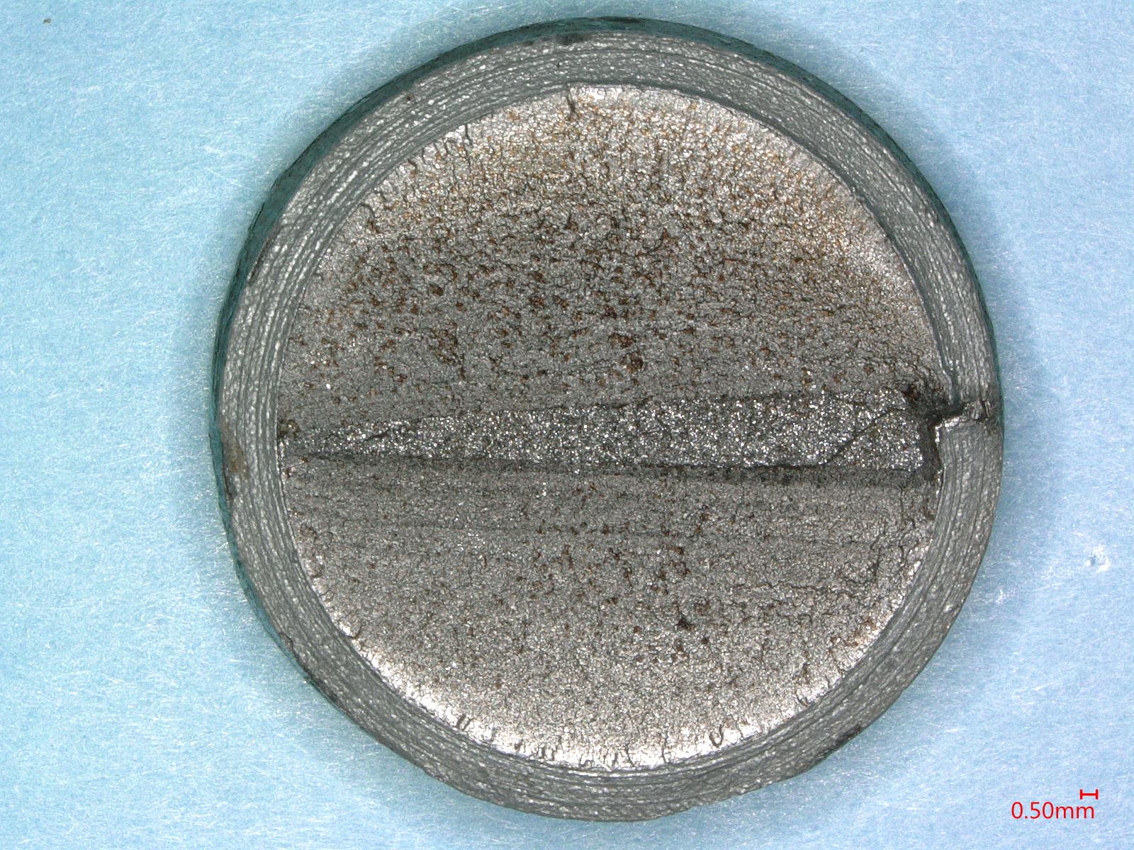 A small silver object featuring a central hole, reflecting light and showcasing its metallic surface.