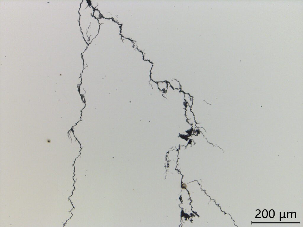 Cracks in a thin material are shown under microscopic view, highlighting structural integrity issues. The scale bar indicates dimensions of 200 micrometers.